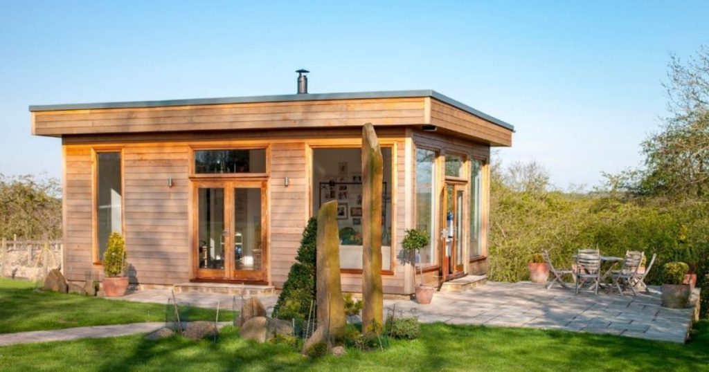 Een vrijstaande tuinveranda uit hout in een groene tuin met aangrenzend tegelterras.