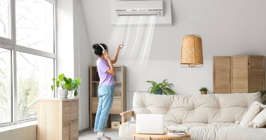 Een dame in paars t-shirt en jeansbroek gebruikt een afstandsbediening om de temperatuur in te stellen op de witte wandairco van haar vaste single-split airco systeem.