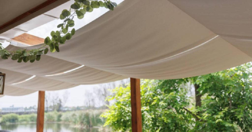 Een houten veranda met glazen dak en zonwerend doek.