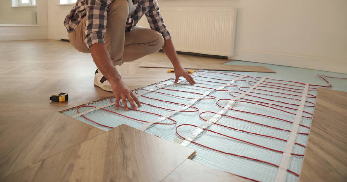 Een installateur plaatst vloerverwarming onder een laminaatparket in een kleine woonruimte. De vloerverwarming is aangesloten op een warmtepompboiler.