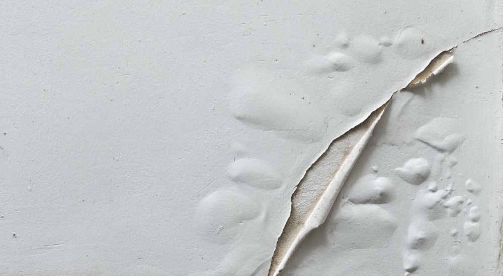 Een vochtige witte muur waarbij het behang loslaat.