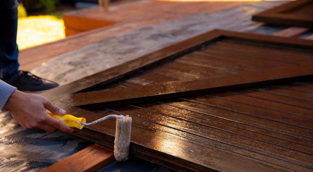 Er wordt vochtwerende verf of coating aangebracht op een paneel van een houten schuur.