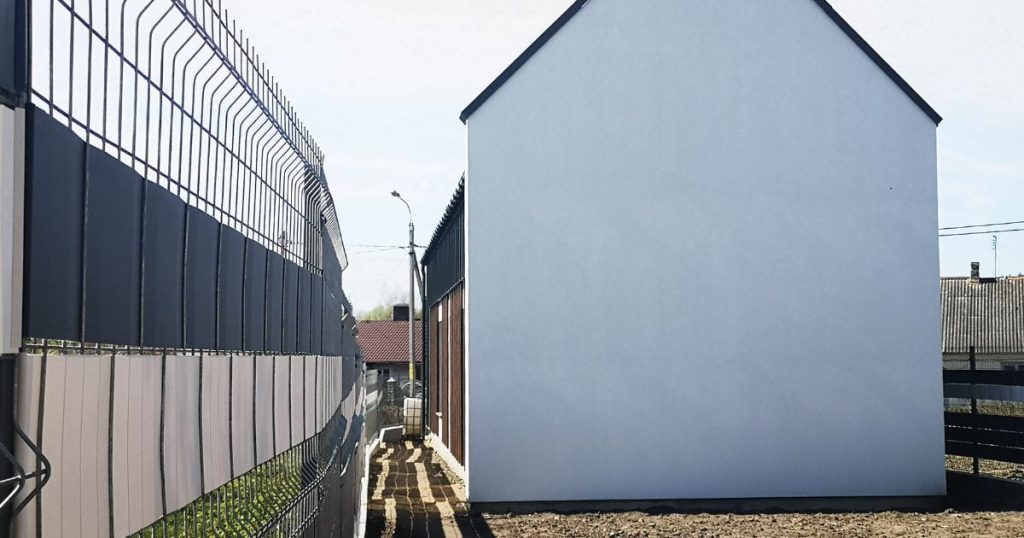 Een witte wachtgevel naast een rijtjeswoning. Voor de woning staat een hek.