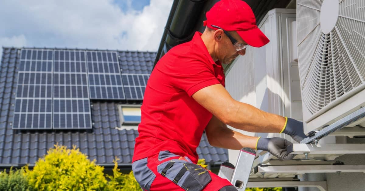 Een specialist in rode kleding installeert een warmtepomp aan de buitenkant van een woning.