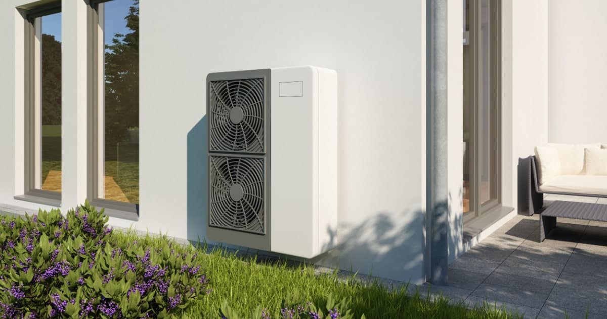 omkeerbare warmtepomp buiten huis bevestigd aan een witte muur boven het gras