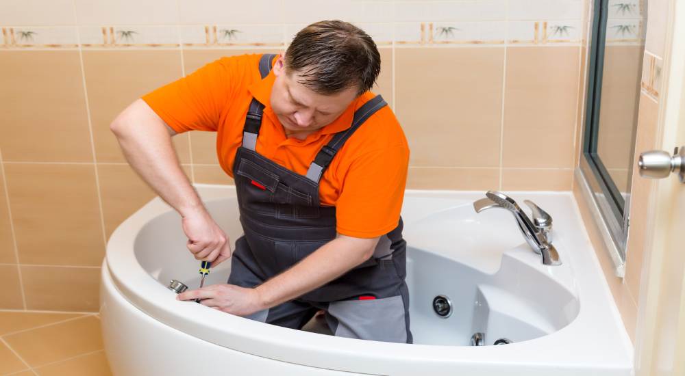 Een badkamerspecialist installeert een zitbad in de hoek van een betegelde badkamer.