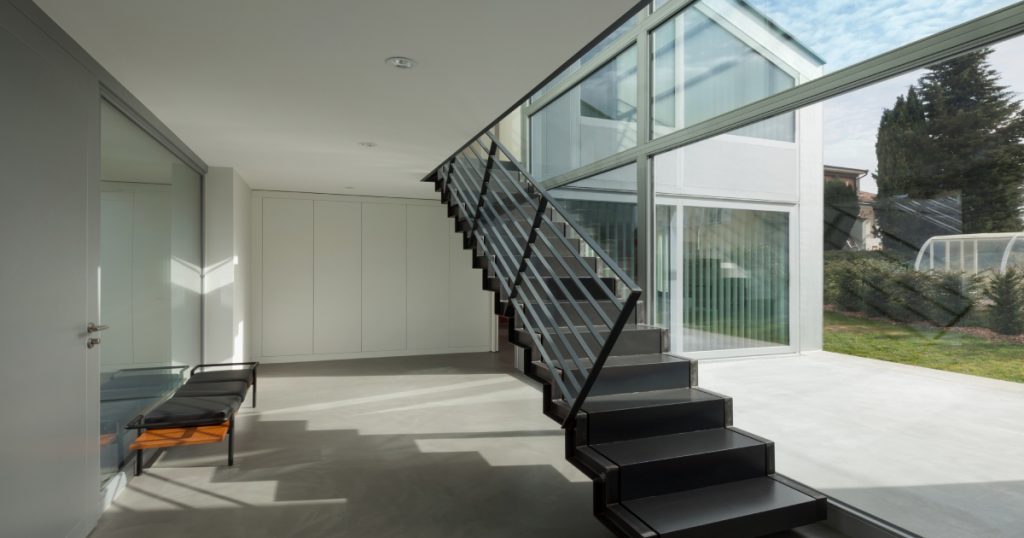 Een grijze betonlook trap met een grijze metalen leuning in een licht interieur