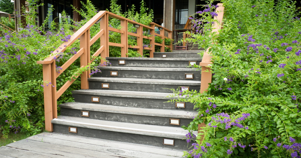 Een grijze tuintrap met houten leuningen