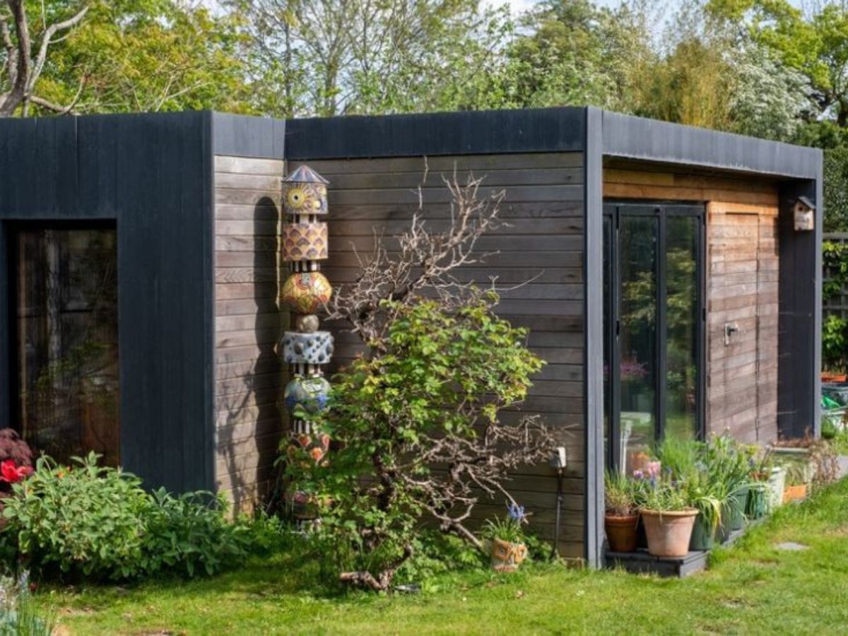 Moderne tuinwoning met horizontale en verticale houten gevelbekleding en grote glazen schuifdeuren, omgeven door planten en tuin.