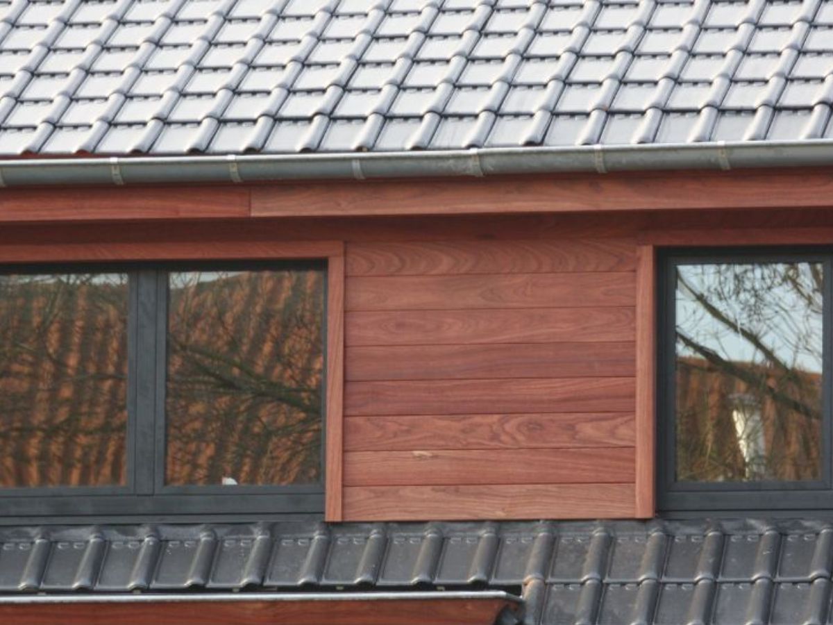 Padoek gevelbekleding met zwarte kozijnen en ramen, bovenaan een dakbedekking met zwarte dakpannen.