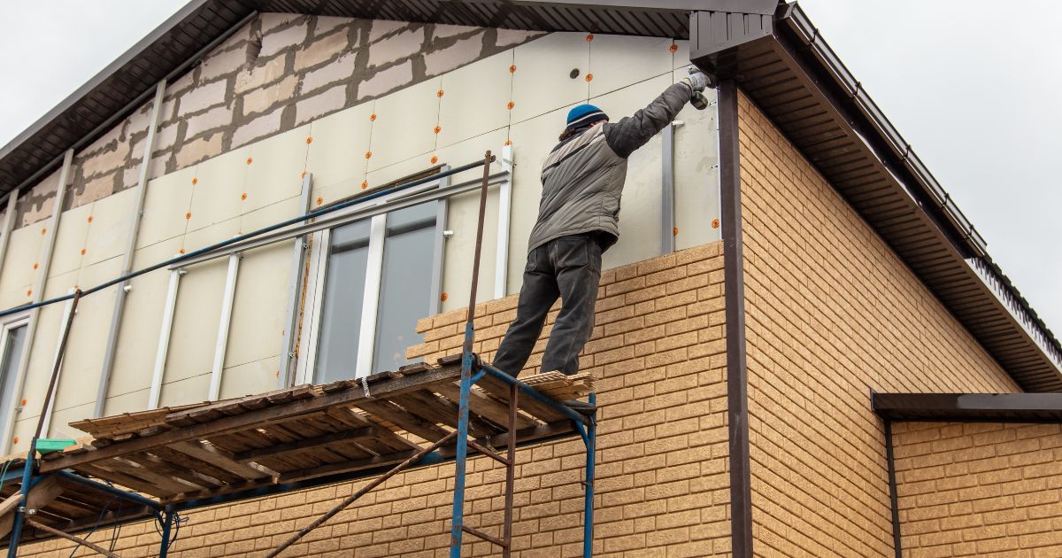 Een gevelwerker brengt steenstrips aan op de gevel van een woning tijdens een renovatie met isolatie.