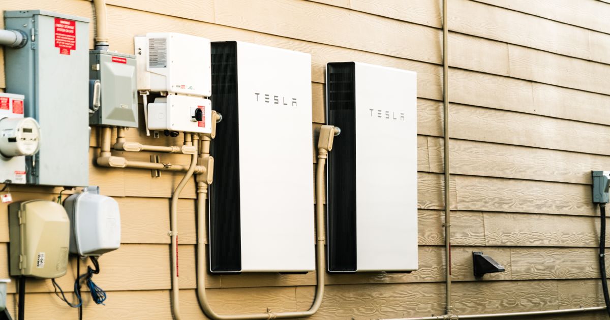Twee Tesla Powerwall thuisaccu's aan een houten buitenmuur, gemonteerd door een Tesla installateur.