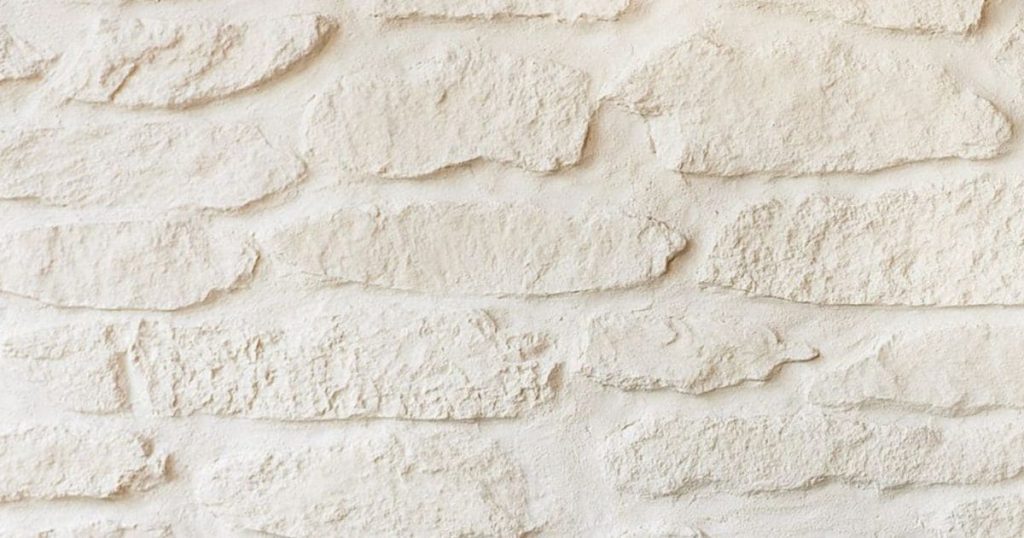 Een beige gevel met sierpleister en een baksteenmotief