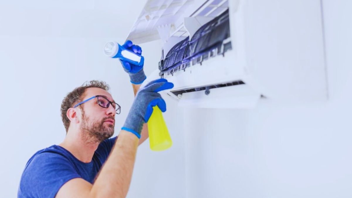 Een man reinigt de binnenunit van een airco. Hij gebruikt hiervoor een zaklamp en draagt beschermende handschoenen.