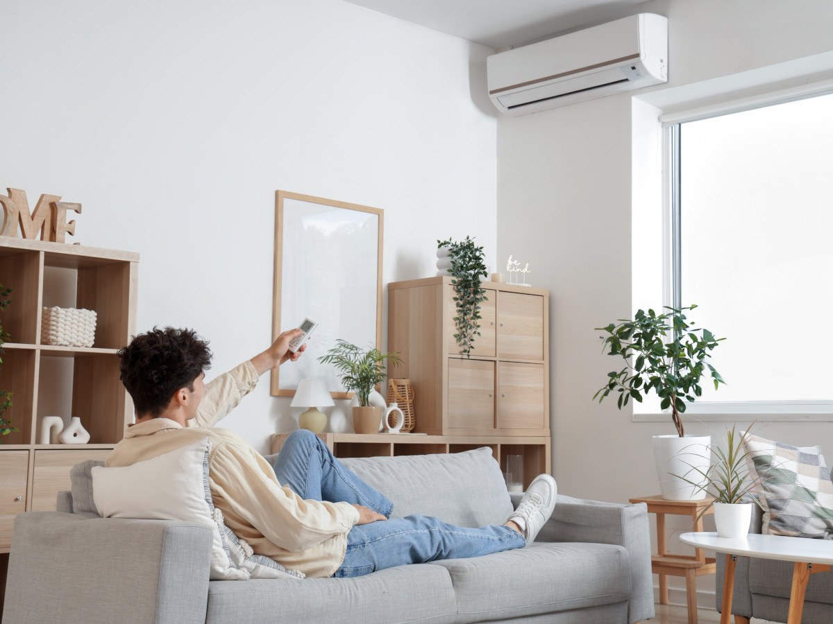 man op bank zet airconditioner aan met afstandsbediening voor verwarming
