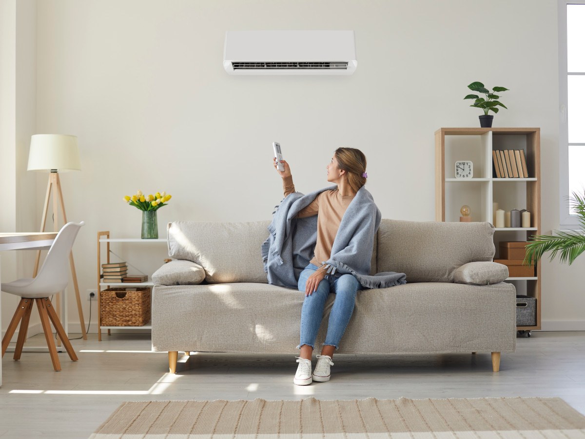 Vrouw met deken over schouders op bank stelt de airconditioner opnieuw in voor verwarmen