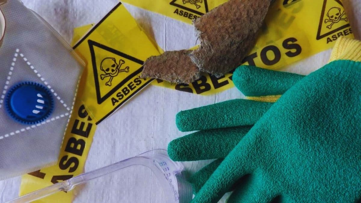 Een witte ondergrond met daarop beschermende asbest handschoenen, een masker, asbestlint en een stuk asbest.