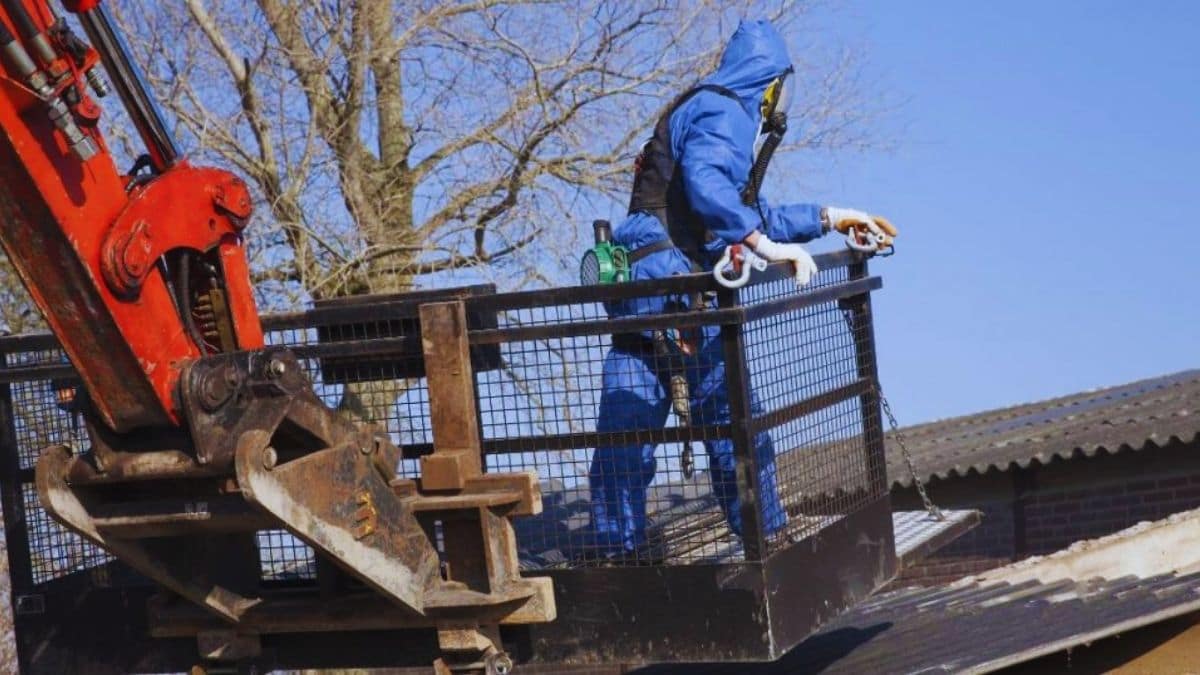 Een asbestspecialist in een blauw beschermingspak verwijdert een asbestdak.