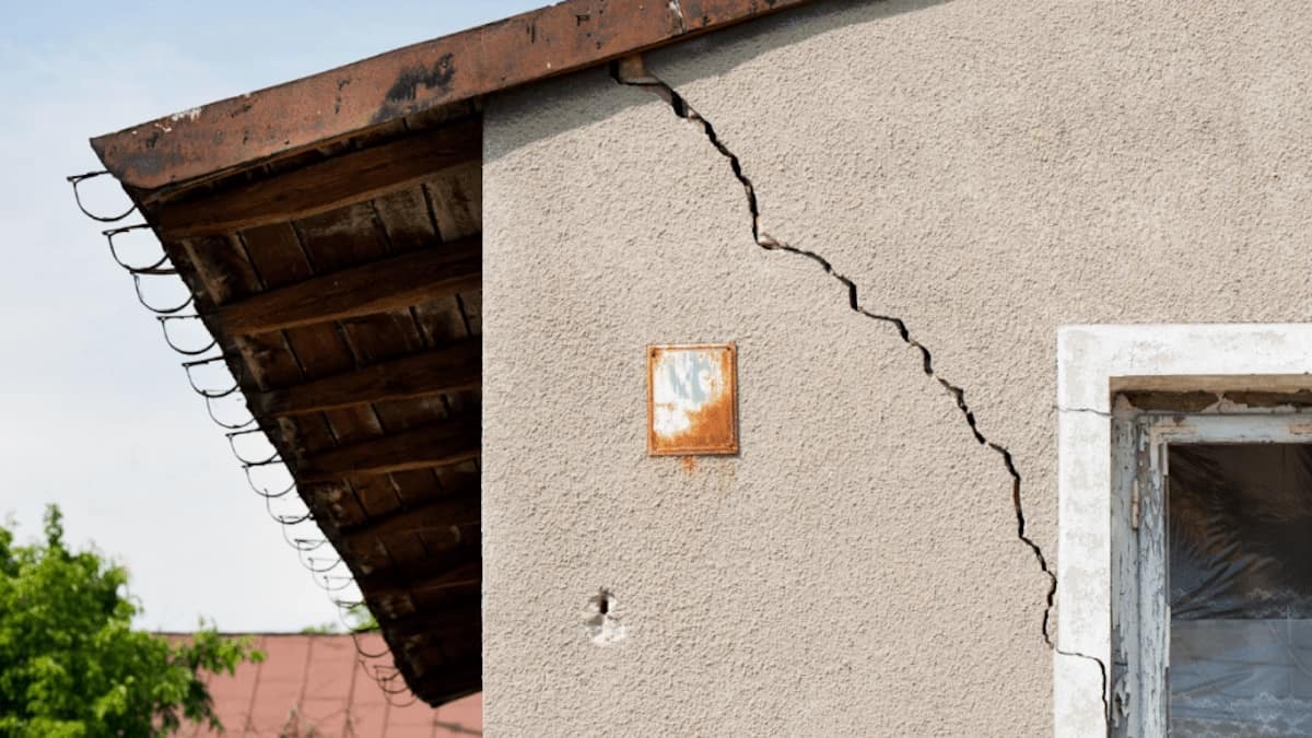 Een diagonale of schuine scheur in een gevel van sierpleister. De scheur is ongeveer een centimeter breed.