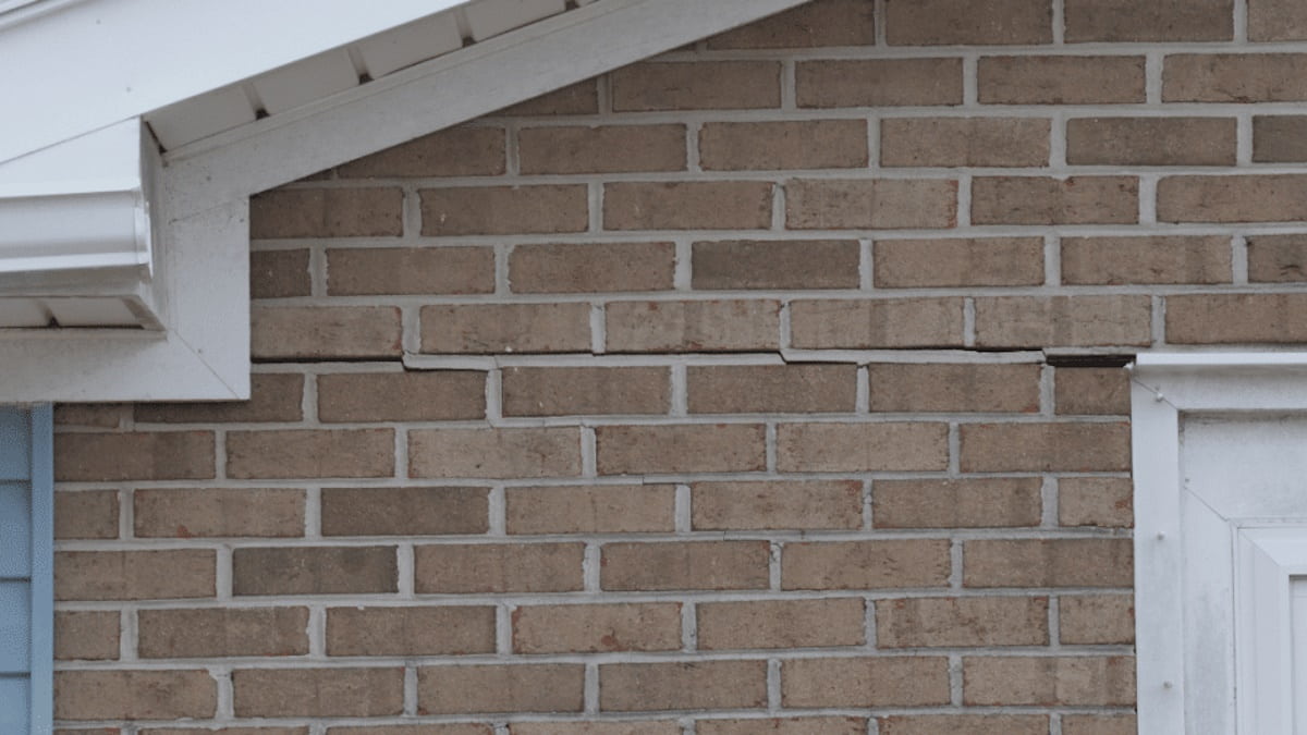 Een horizontale scheur in de voeg van een bakstenen gevel. De scheur loopt vanaf het dak tot aan het deurkozijn.