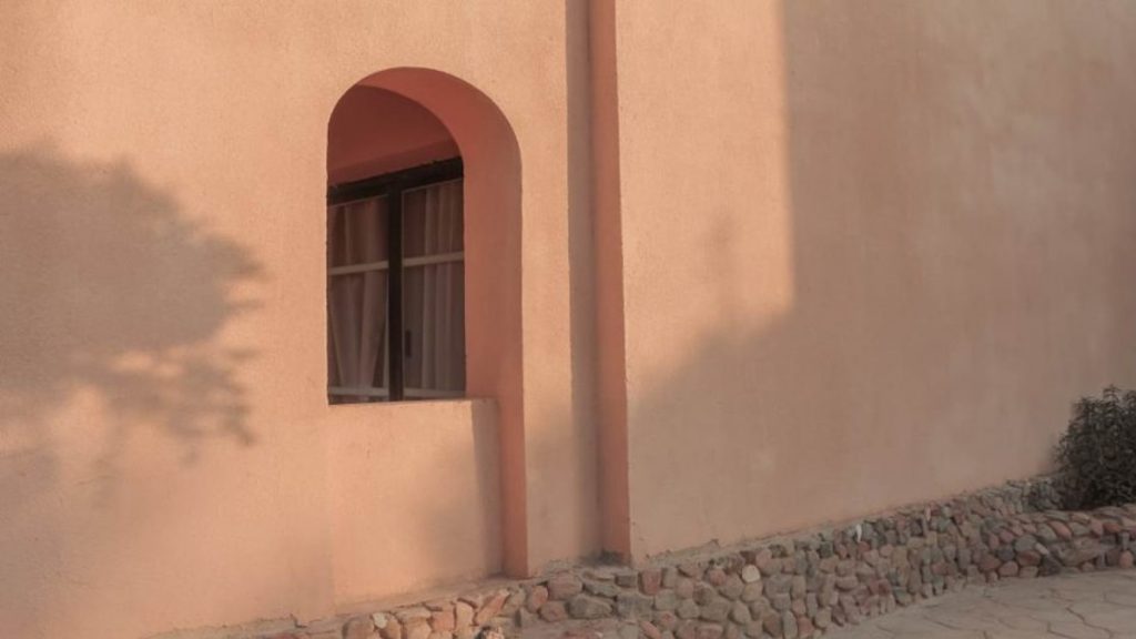 De zon schijnt op een beige gevel, gemaakt van sierpleister. In de gevel is een nis in de vorm van een boog zichtbaar.