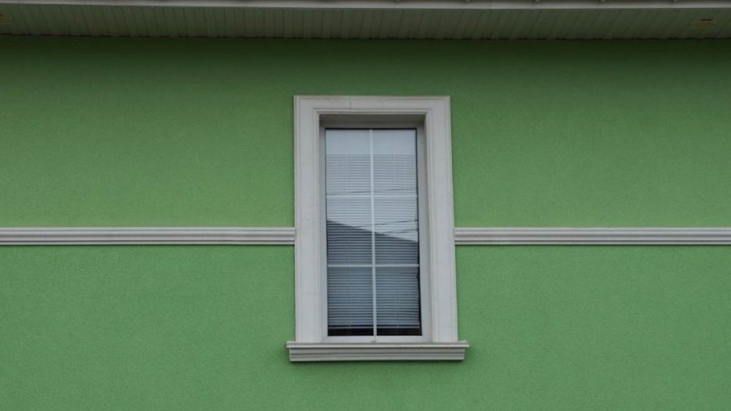 Een groene sierpleister gevel, op de foto is een raam zichtbaar.