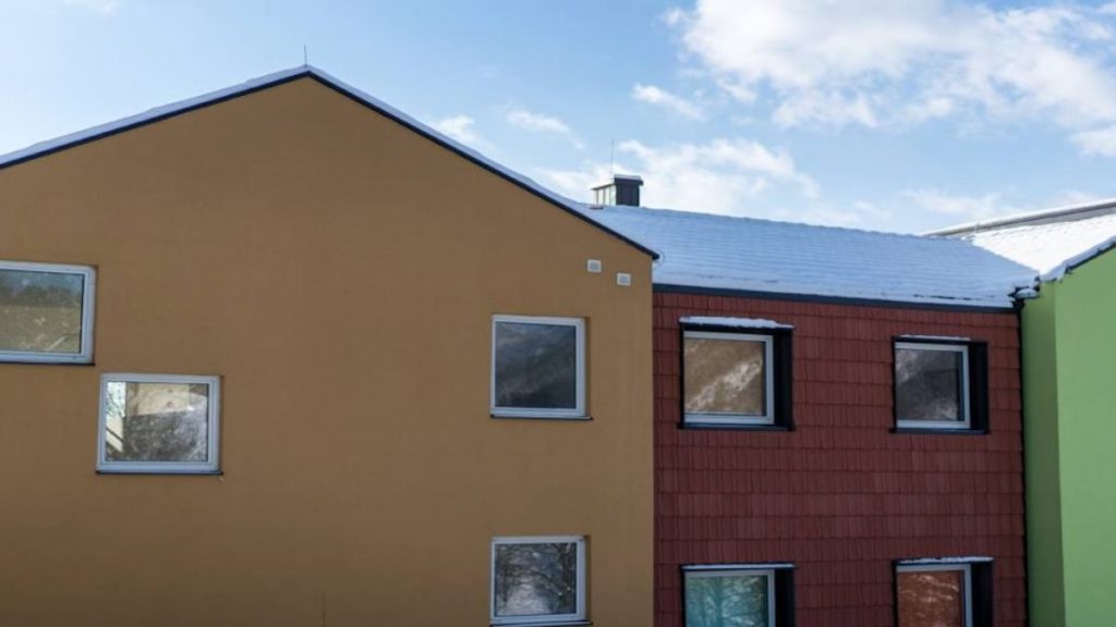 Een beige sierpleister gevel in een donkere tint. Naast de beige gevel zijn een rode en een groene gevel zichtbaar.