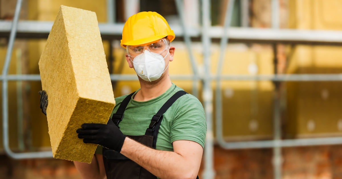 Een isolatiespecialist draagt een blok spouwmuurisolatie gemaakt van minerale wol. De expert draagt beschermende kleding