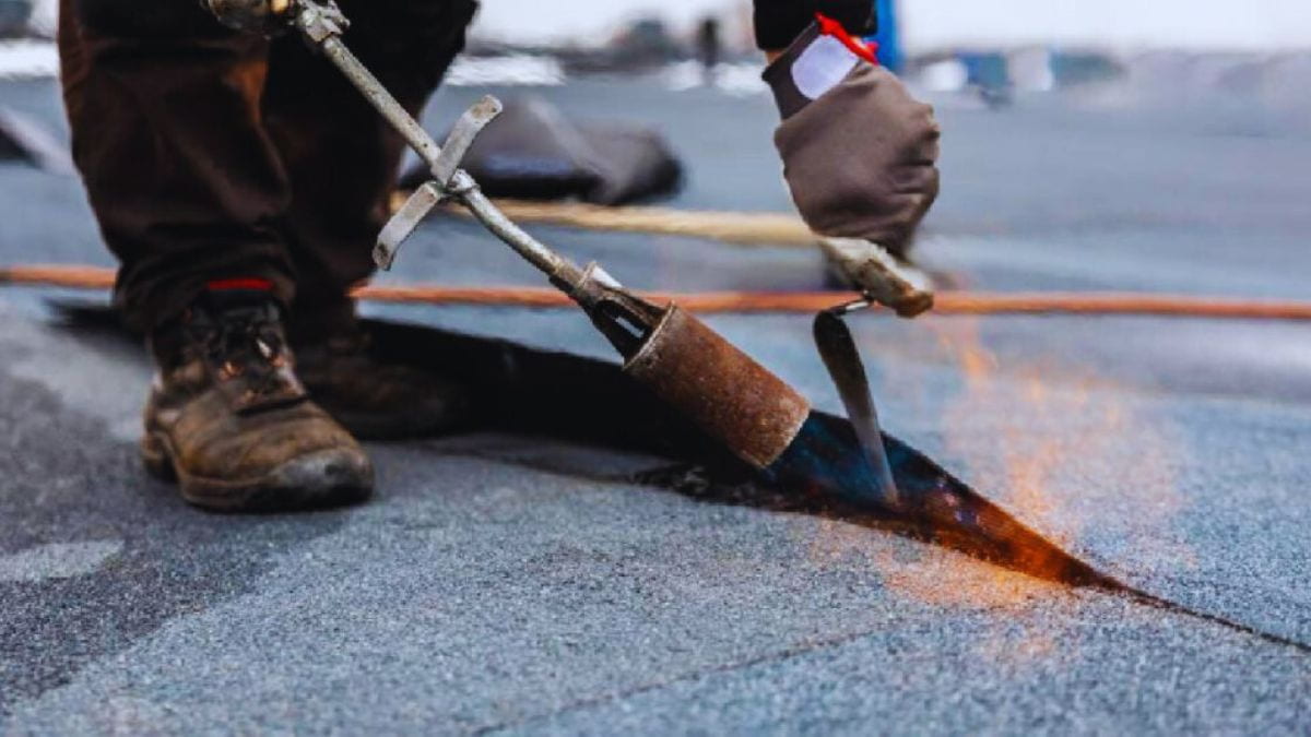 Een dakwerker gebruikt een brander om bitumen dakbedekking aan het dak te hechten.