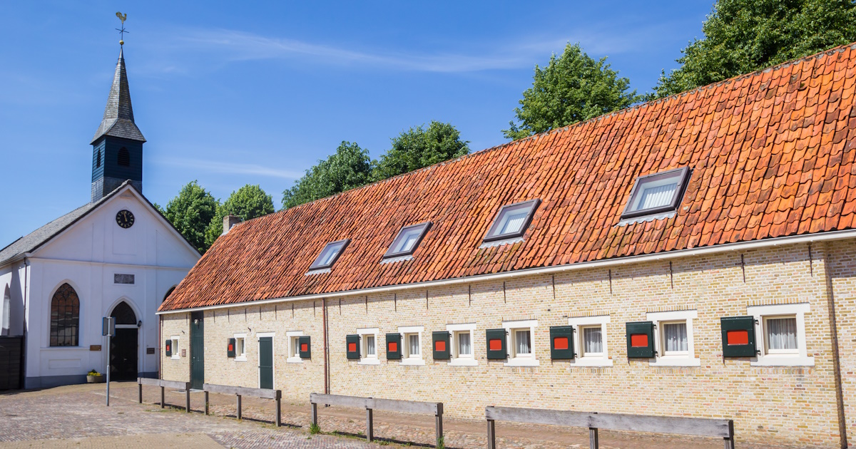 Een gebouw met klassieke boomse pannen op het dak, op de achtergrond een kerk