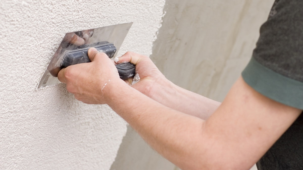 Een man gebruikt een spaan om een sierpleister op de gevel aan te brengen. 