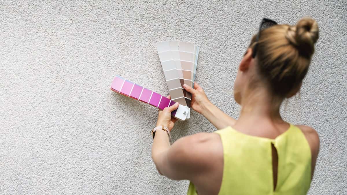Een vrouw gebruikt een kleurenwaaier om te bepalen welke kleur de bepleistering op de gevel krijgt.