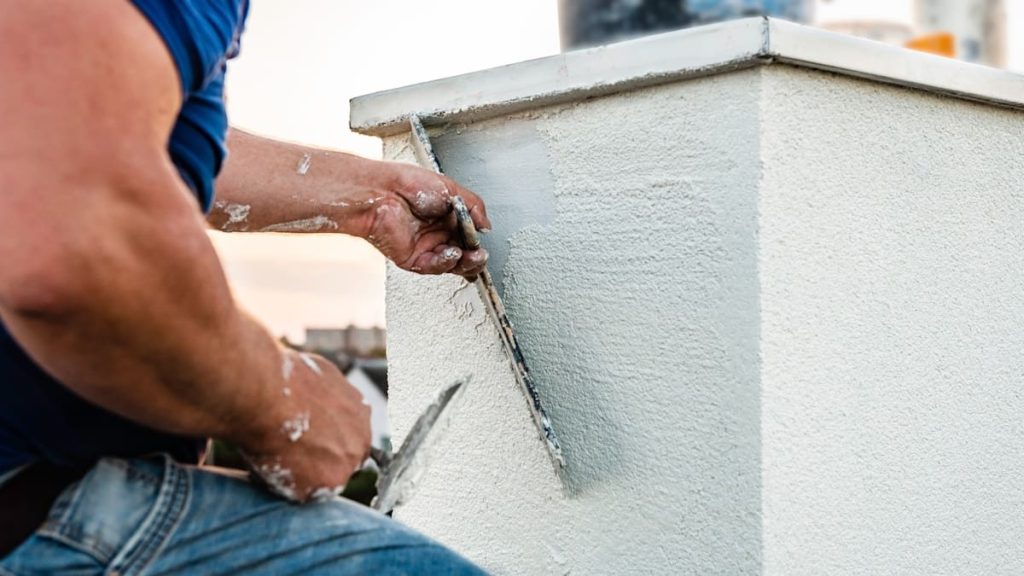 Een man brengt sierpleister aan met een spaan. De armen van de man zitten onder de stucvlekken.