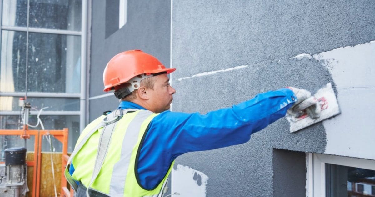 Een vakman is bezig met het stucen van een buitenmuur.