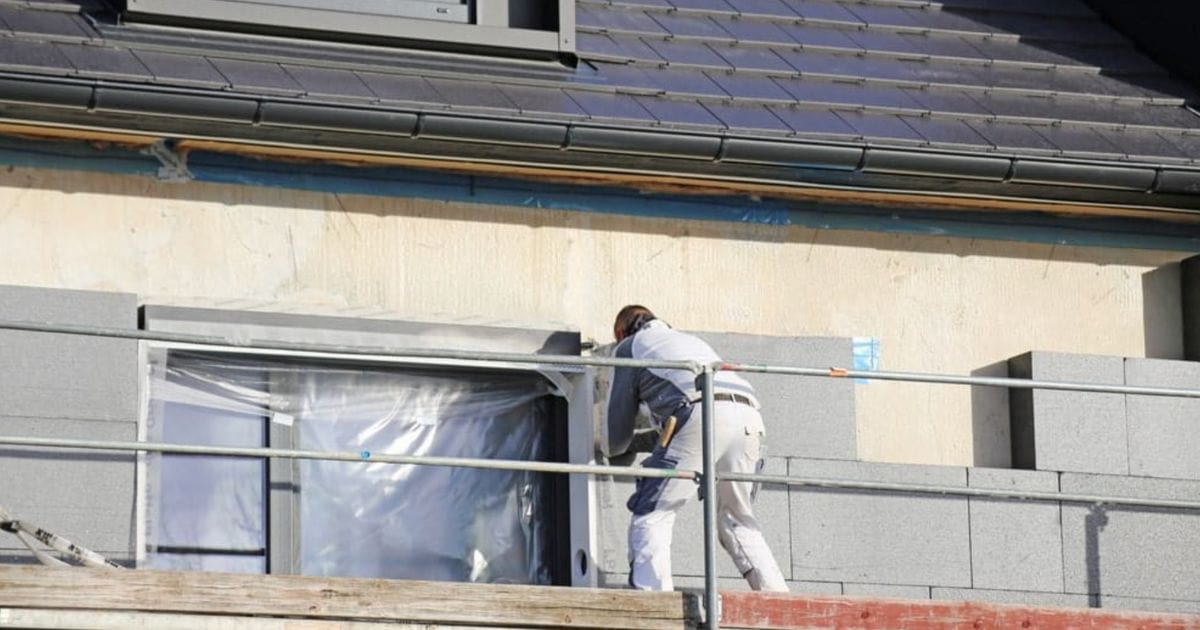Een vakman staat op een steiger en is bezig met de isolatie van een buitenmuur