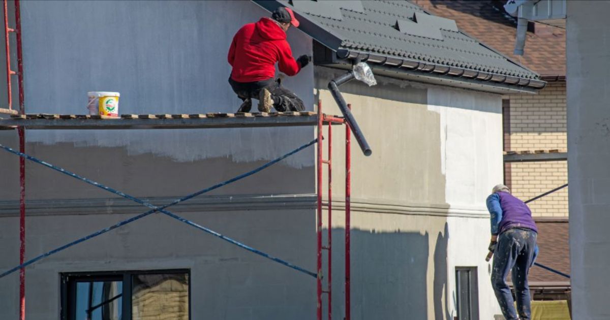Twee vochtbestrijders zijn op een steiger de buitenmuur waterdicht aan het maken met vochtwerende verf.