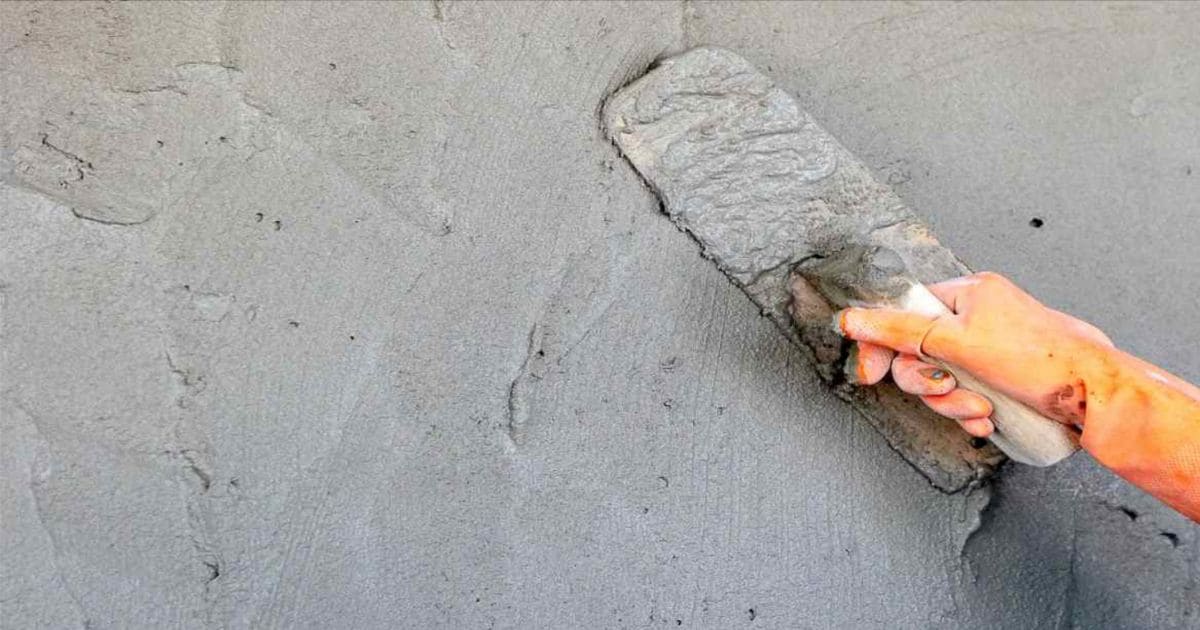 Een vakman met een oranje handschoen is cementpleister aan het aanbrengen op een muur
