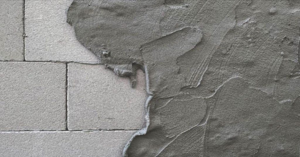 Een muur is voor de helft bedekt met een dikke laag grijze cementpleister