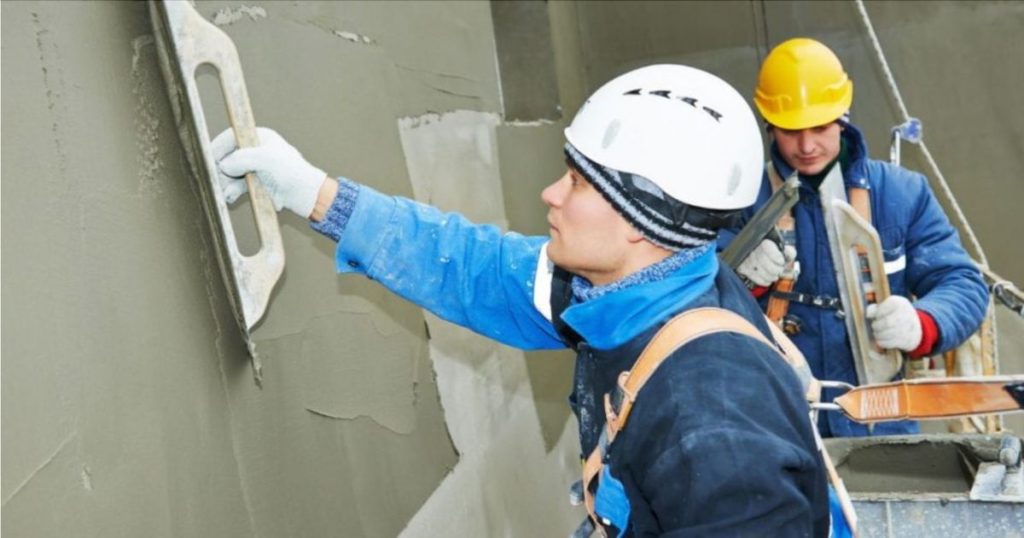 Twee vakmannen zijn een primer op een muur aan het aanbrengen als voorbereiding op de cementpleister