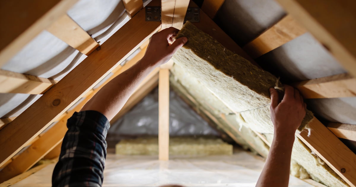 Een dakdekker plaatst matten isolatiemateriaal tegen de binnenzijde van het dak