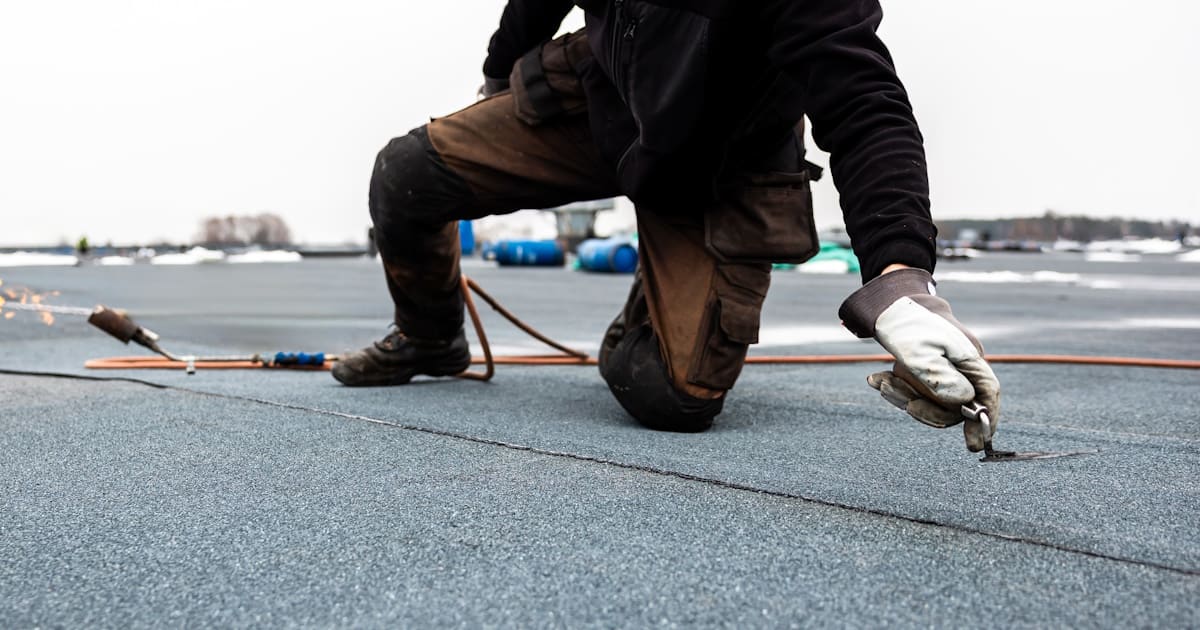Een dakdekker drukt de naden van een strook bitumen dakbedekking aan voor een waterdichte verbinding
