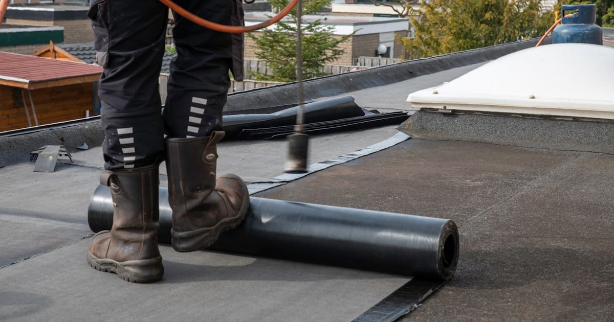 Een dakdekker gebruikt een brander om een strook dakleer aan het dakoppervlak te hechten