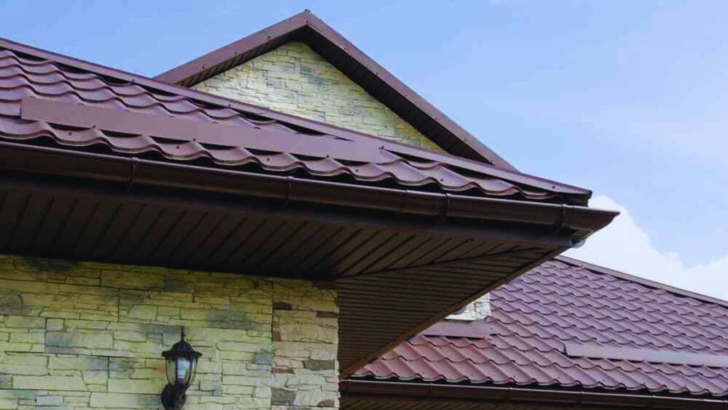 Een dakoverstek bij een woning met grijze dakpannen. De dakoverstek is onder de dakgoot geplaatst en ook in de bruine kleur uitgevoerd.