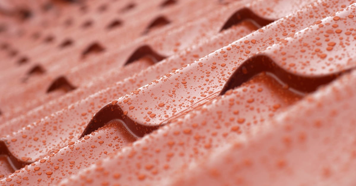 Een close-up van regendruppels op keramische dakpannen met een rode kleur.