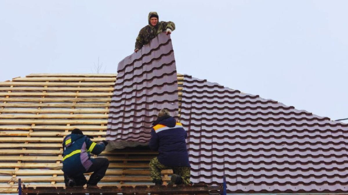 Drie dakspecialisten werken samen om een dakpanplaat met isolatie op de panlatten van een dak te leggen.