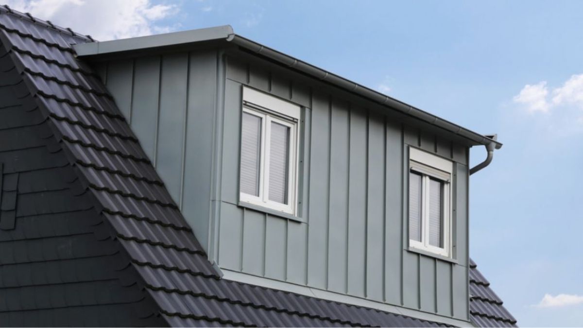 Dakrand met zinken gevelpanelen, witte kozijnen en ramen in een moderne woning, tegen een blauwe lucht.