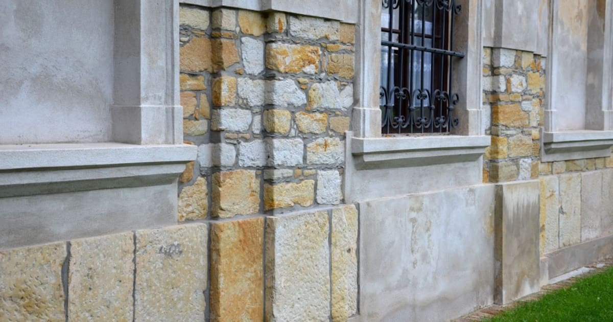 De stenen gevel van een woning. De stenen zijn onregelmatig van vorm en kleur. De gevel wordt gecombineerd met klassieke elementen.