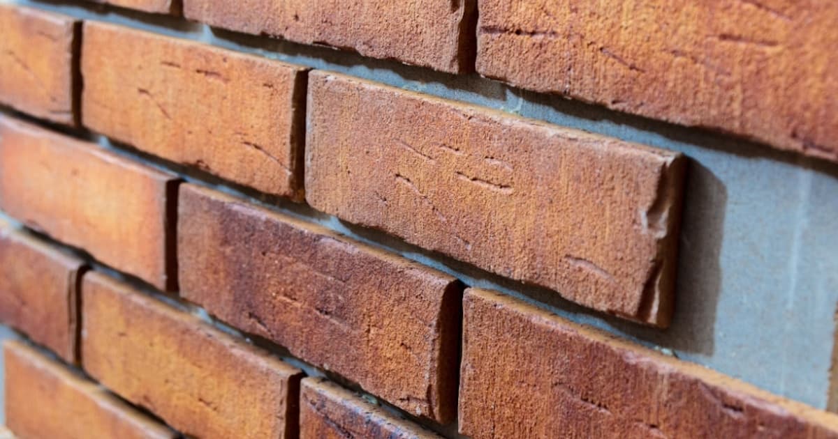 Een close-up van rode steenstrips tegen een gevel. Doordat rechts nog een steenstrip ontbreekt kun je goed de geringe dikte zien. 