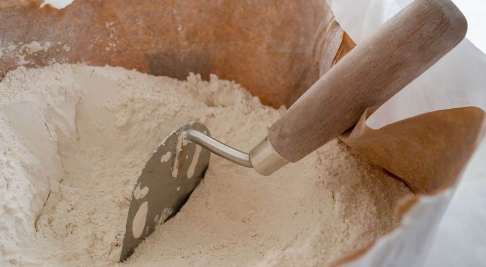 Een witte papieren zak met gebluste kalk waarin een metalen schepje met houten handvat zit.