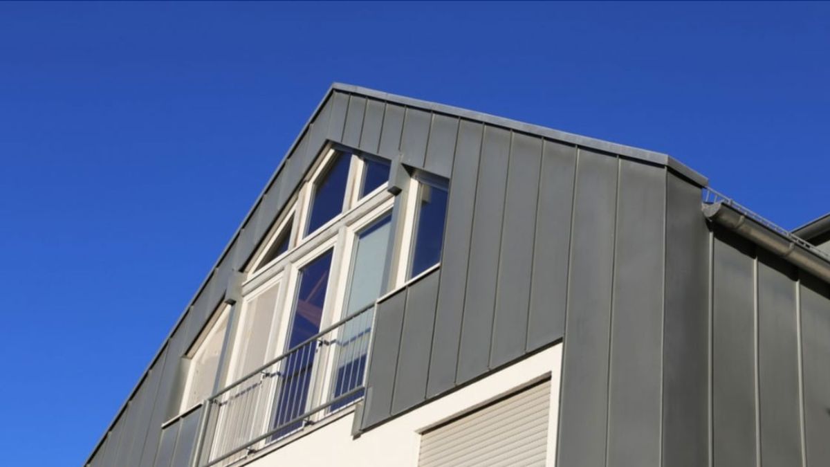 Detail van een woning met zinken gevelpanelen en een helderblauwe lucht op de achtergrond.